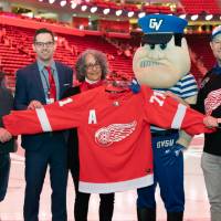 Alumni pose with Louie the Laker while holding up a Red Wings Jersey at the Detroit Red Wings GVSU Night
